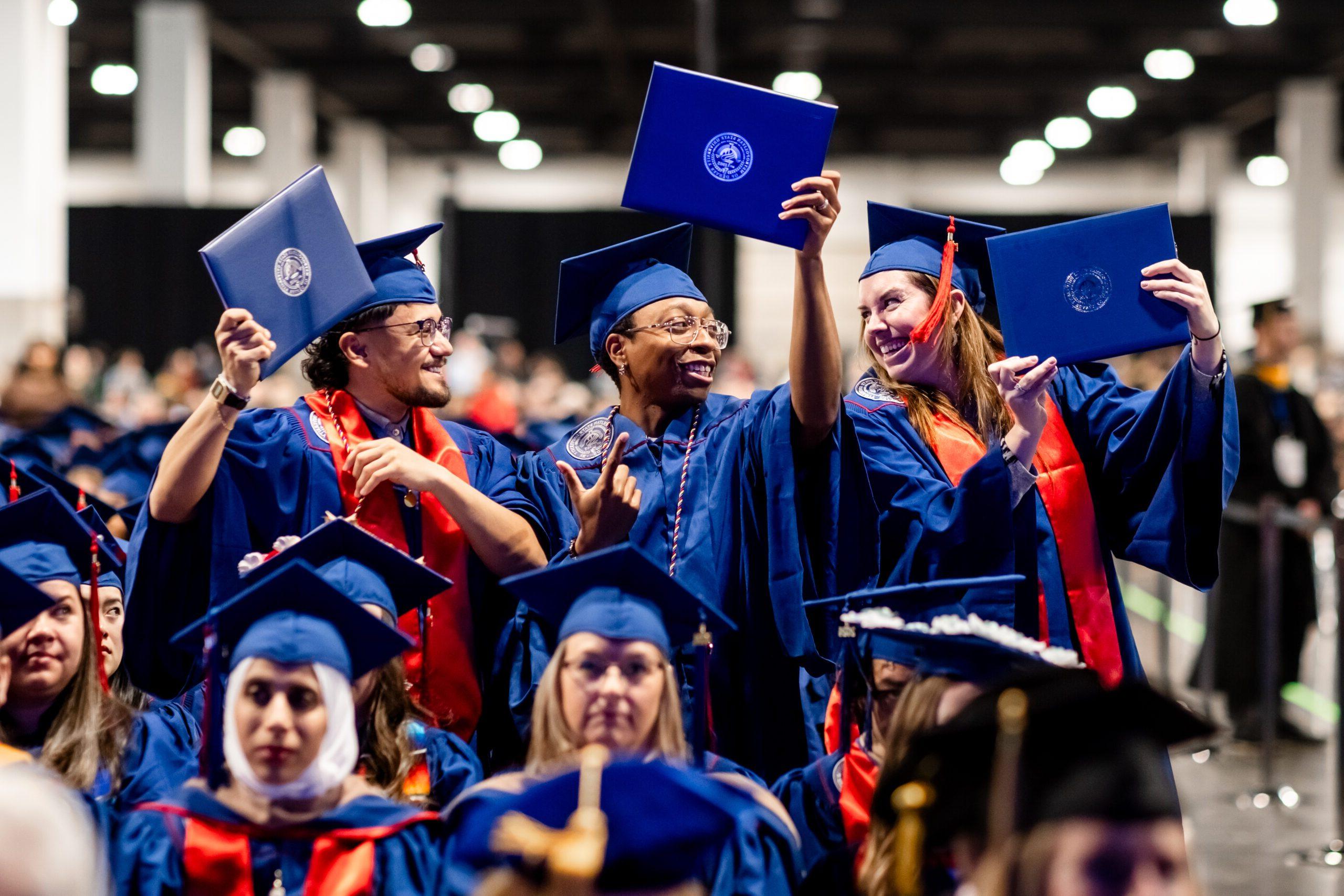 3 accounting graduates elated after crossing the stage holding up their diploma covers and talking with each other before taking their seat